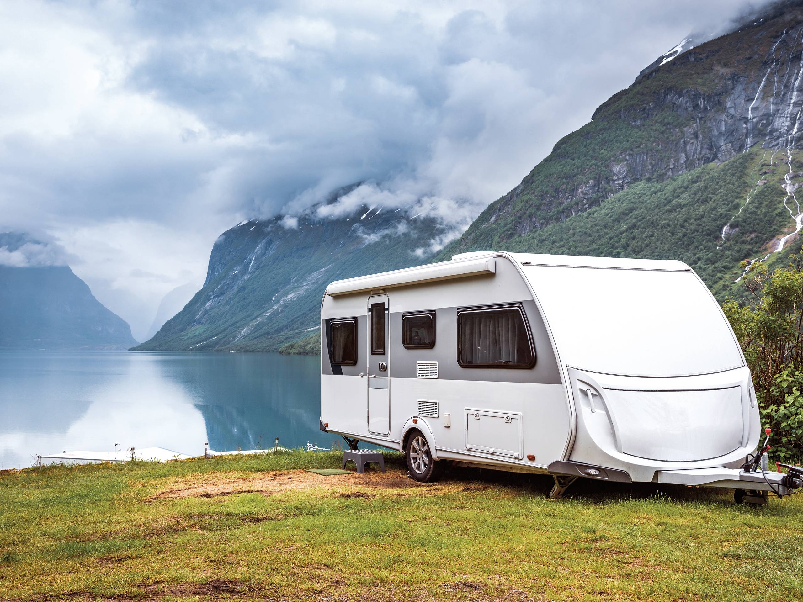 Wohnwagen steht am See. Im Hintergrund Berge.